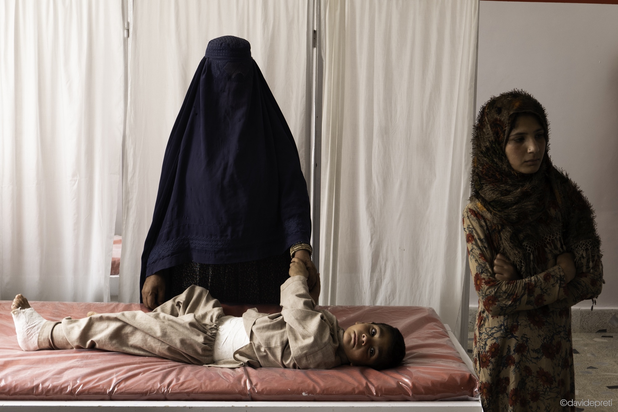 Kabul, Afghanistan — July 19, 2021.

A family waits for the doctor to arrive for a dressing at EMERGENCY's FAP (First Aid Post) in Mirbachakor. Access to healthcare is extremely difficult for much of the Afghan population: there are few free healthcare facilities, and the country's geography can make travel to medical centres challenging. EMERGENCY has established a network of FAPs connected to its hospitals through a 24-hour ambulance service.
