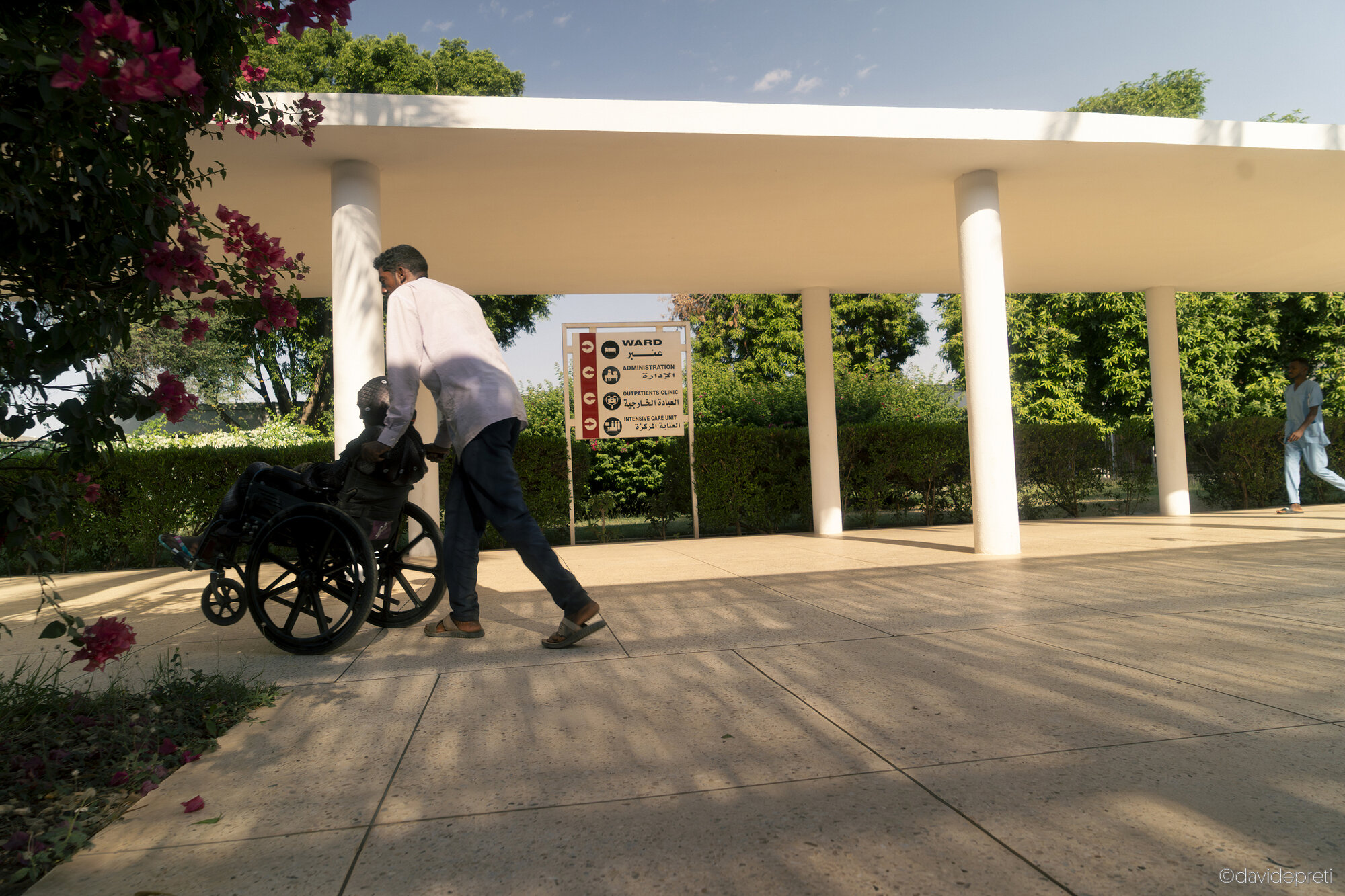Khartoum, Sudan — November 23, 2025.

A patient in a wheelchair and a companion head toward the inpatient wards at EMERGENCY's Salam Centre for Cardiac Surgery.
