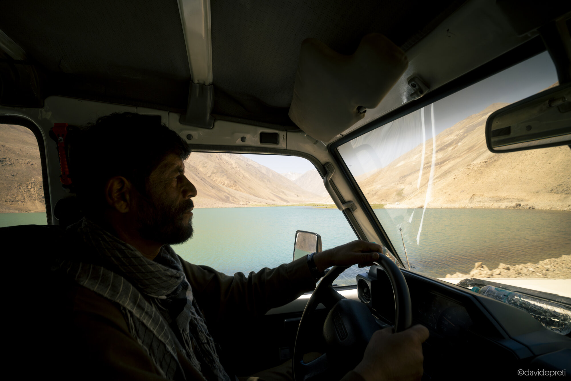 Badakhshan Valley, Afghanistan — July 11, 2025.

A view from inside a vehicle navigating a dusty, unpaved mountain road as it winds along a river canyon towards the remote village of Anjuman in Badakhshan province.
